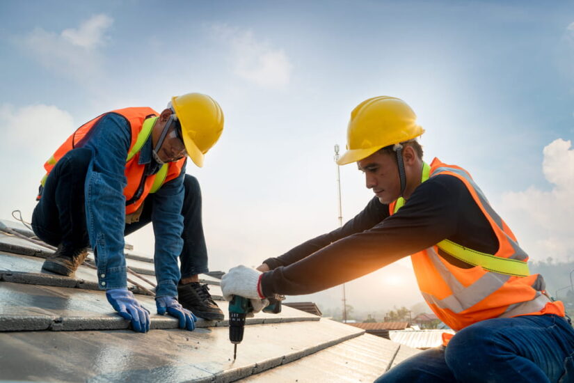 Two Workers Drilling Asphalt Shingles To The Roof