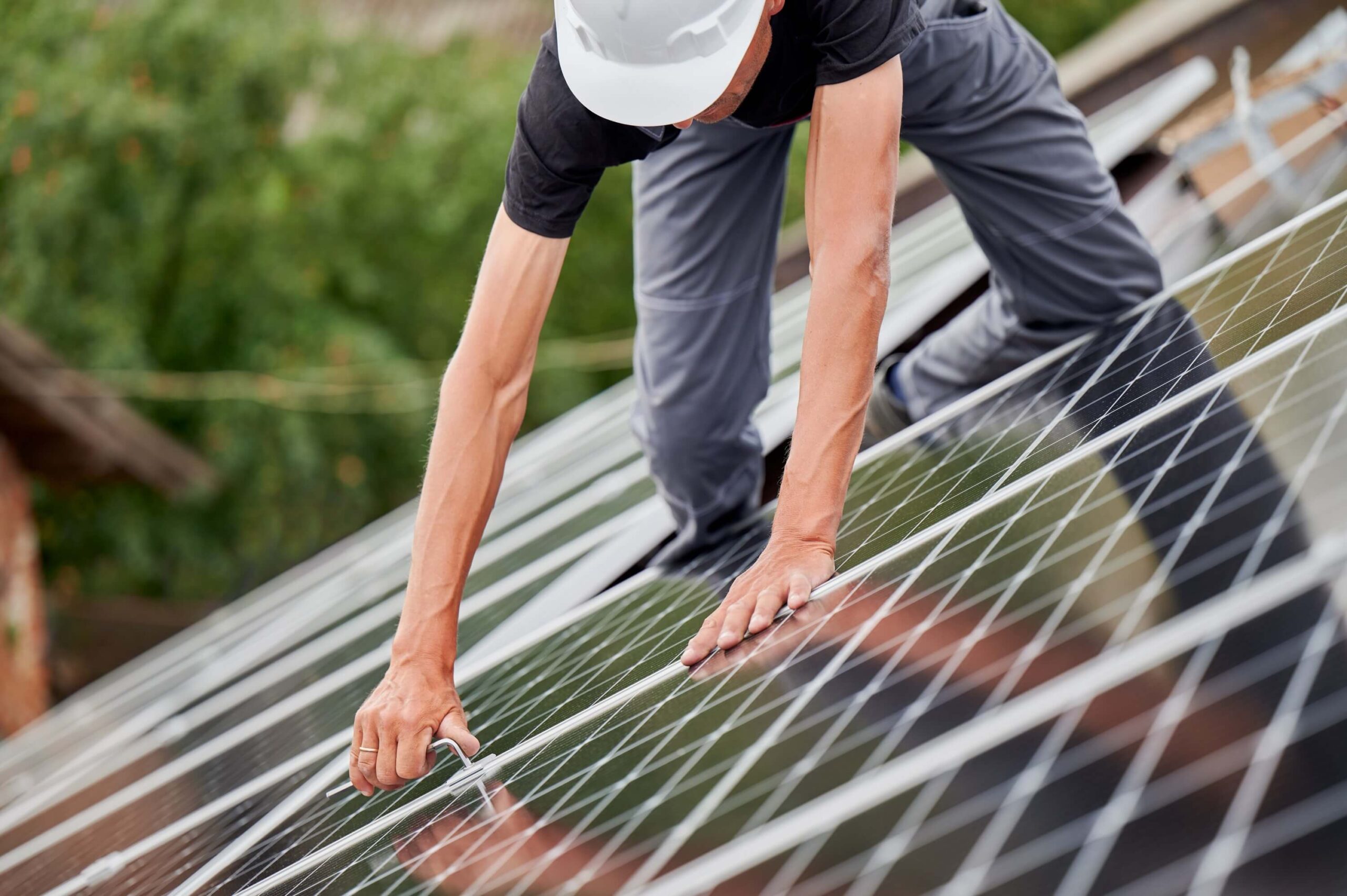 Technician man mounting photovoltaic solar modules on house roof.